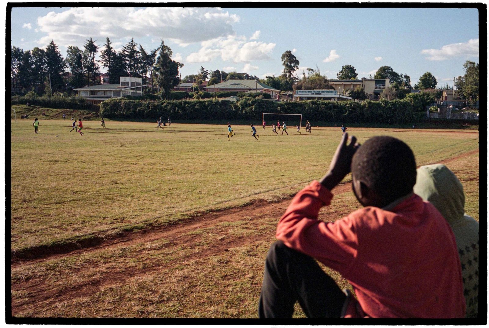 Deux jeunes frères observent un match de soccer, leurs chaussures trouées les empêchant d’y participer.