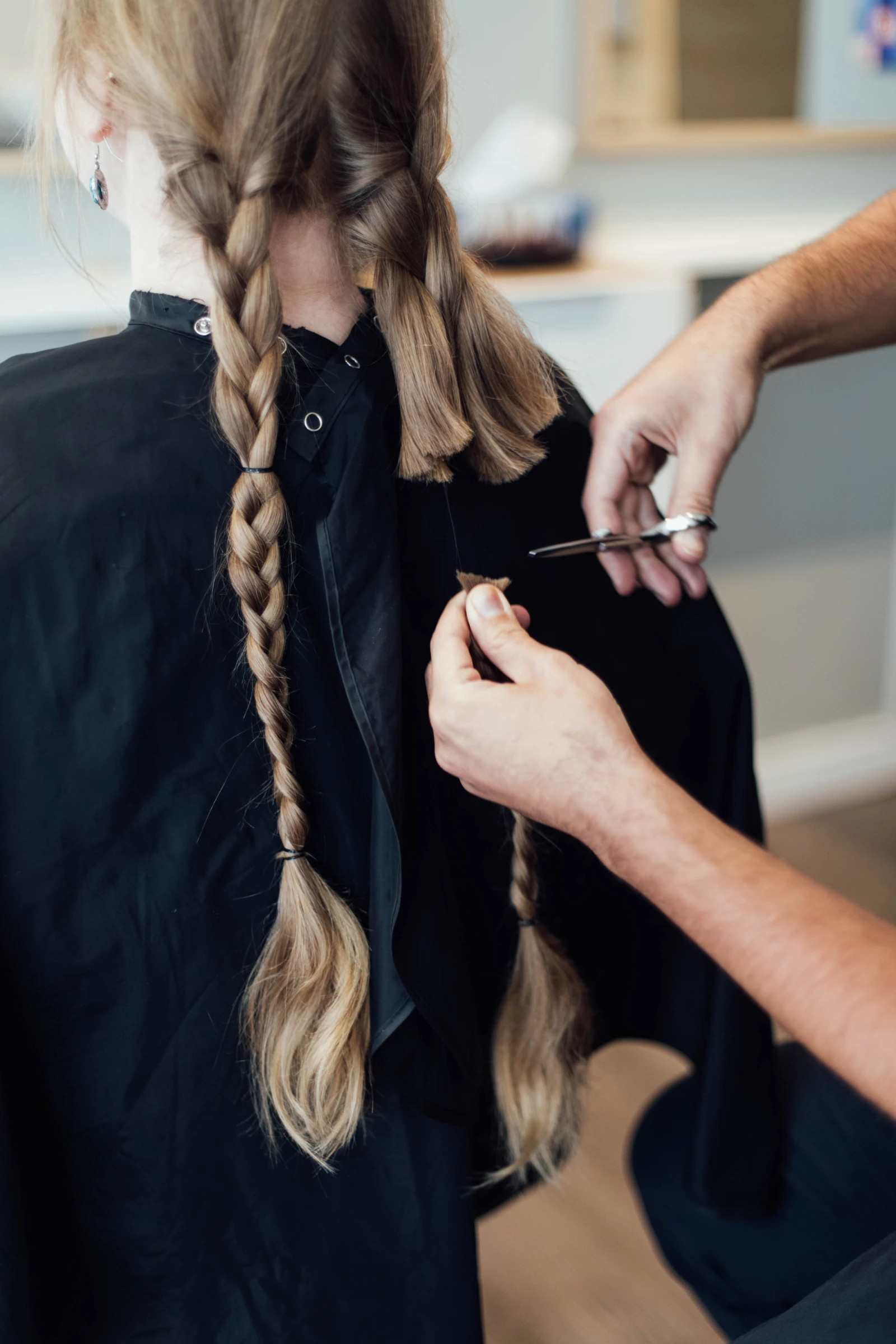 C POUR « COIFFER », PAS POUR « CONSEILLER »   Indiana a sorti une photo d’elle avant les traitements pour aider Louise à faire un premier choix parmi les perruques alignées sur le mur. Cette dernière jette un œil, hoche la tête et se dirige illico vers la tablette du bas derrière elle. Visiblement, elle connaît l’inventaire par cœur. « Ah ! Voilà celle que je cherchais. On va commencer par celle-là ! » D’un geste assuré, elle dépouille la tête en styromousse de sa prothèse, secoue la masse de cheveux synthétiques, place quelques mèches, tend le bras et regarde le résultat de loin pour avoir une vue d’ensemble. Oubliez le stéréotype de la « moumoute » qui se voit à 8 km de distance (allô, Daniel Lavoie, dans l’inoubliable minisérie Félix Leclerc des années 2000 !) : ici, naturelles ou pas, les perruques sont toutes « bluffantes » de réalisme. « On est chanceux d’avoir des prothèses d’aussi bonne qualité. Habituellement, cette qualité-là se paye cher », dit Louise. Une perruque haut de gamme peut effectivement valoir plusieurs centaines, voire des milliers de dollars. « Mais ici, on fonctionne par système de prêt. Pour 20 $, la cliente ou le client pourra conserver la perruque tout le temps nécessaire : trois, sept, neuf mois ou plus. » Elle ajoute : « En bout de piste, on nous la rapporte, on la nettoie et elle peut être prêtée de nouveau. En cours de route, la personne peut aussi décider de changer de perruque. Elle revient et on fait un nouvel essayage. Certains en profitent pour explorer une autre coupe, un autre style, une autre couleur… » Louise est interrompue par Indiana qui ajoute en riant : « Moi, je préfère me ressembler ! »   TCHOP, TCHOP Coupe, style, couleur… C’est aussi ce qui fait jaser une fois de retour à L’Atelier 100. « « Le plus difficile, c’est d’annoncer à une donneuse qu’elle ne pourra pas nécessairement avoir la coupe souhaitée une fois que les ciseaux seront passés par là », me dit Olivier, qui n’en est pas à sa première expérience du genre. Il faut savoir qu’il y a plusieurs critères à respecter pour faire un don de cheveux. Les organismes exigent des cheveux non traités chimiquement (pas de couleur ni de permanente), avec moins de 5 % de gris, et d’une longueur d’au moins une vingtaine de centimètres (8 pouces). « Couper tout ça d’un coup, c’est beaucoup ; il faut s’ajuster », dit le coiffeur. Mais la plupart du temps, ça se passe bien ? « Oui ! Les gens sont tellement engagés dans la démarche ! Je me souviens d’une femme qui avait à peine la longueur nécessaire. On a trouvé une astuce pour en avoir assez en lui faisant une multitude de petites couettes tout autour de la tête — style hérisson ! — plutôt qu’une tresse. À la fin, elle avait pratiquement la tête rasée… et elle était ravie ! »        Je me retourne vers Karine, qui jette un dernier coup d’œil à ses cheveux dans le miroir. « Toute la journée, j’ai été fébrile, mais je sais que c’est le bon moment. Si j’attends encore, ils vont finir par être endommagés, et je tiens à ce qu’ils soient beaux pour en tirer le maximum. Ça fait tellement longtemps que j’en prends soin ! Quand ma tante a reçu son diagnostic de cancer, l’an dernier, je m’étais promis de donner mes cheveux. C’est aujourd’hui que ça se passe. »    Pendant un moment, j’ai l’impression qu’elle va prendre les jambes à son cou. Elle n’a pas coupé ses cheveux, ou si peu, depuis 2010 ; ils lui vont maintenant au milieu du dos. Peut-être a-t-elle changé d’avis ?    Olivier lui dit un ou deux mots d’encouragement et lui fait un bref câlin. Karine s’apprête à s’asseoir dans sa chaise, puis elle se ravise brusquement. Pendant un moment, j’ai l’impression qu’elle va prendre les jambes à son cou. Elle n’a pas coupé ses cheveux, ou si peu, depuis 2010 ; ils lui vont maintenant au milieu du dos. Peut-être a-t-elle changé d’avis ? Au salon, le temps, dans le mépris le plus complet de la physique quantique, s’est arrêté. « Prendrais-tu une dernière photo de mes tresses ? » Fiou ! Ce n’était que ça.   MIROIR, MIROIR Dans le monde de la prothèse capillaire, il y a le synthétique et le naturel. En s’avançant vers Indiana, Louise m’explique. « Le synthétique, c’est simple : laver, sécher, porter. Le style restera toujours le même et l’entretien est réduit au strict minimum. Mais — et c’est un « mais » important — ça réagit très mal à la chaleur. Par exemple, si tu t’approches trop près d’un four en cuisinant, ça fond ! Ça ne risque pas d’arriver avec les perruques faites de cheveux naturels. Par contre, celles-ci demandent des soins ; il faut les coiffer. On peut les friser, les teindre, comme on le fait avec nos cheveux. »   Devant le miroir, Indiana essaie une première prothèse, secondée par Louise, qui lui donne des recommandations d’ajustement. « Comptez environ quatre doigts à partir des sourcils : ça vous aidera à placer le haut de la perruque. On ajuste les pointes près des oreilles, sinon c’est là que ça se voit que c’est une perruque. Ne reste qu’à placer le bonnet… On coiffe délicatement, et voilà ! »