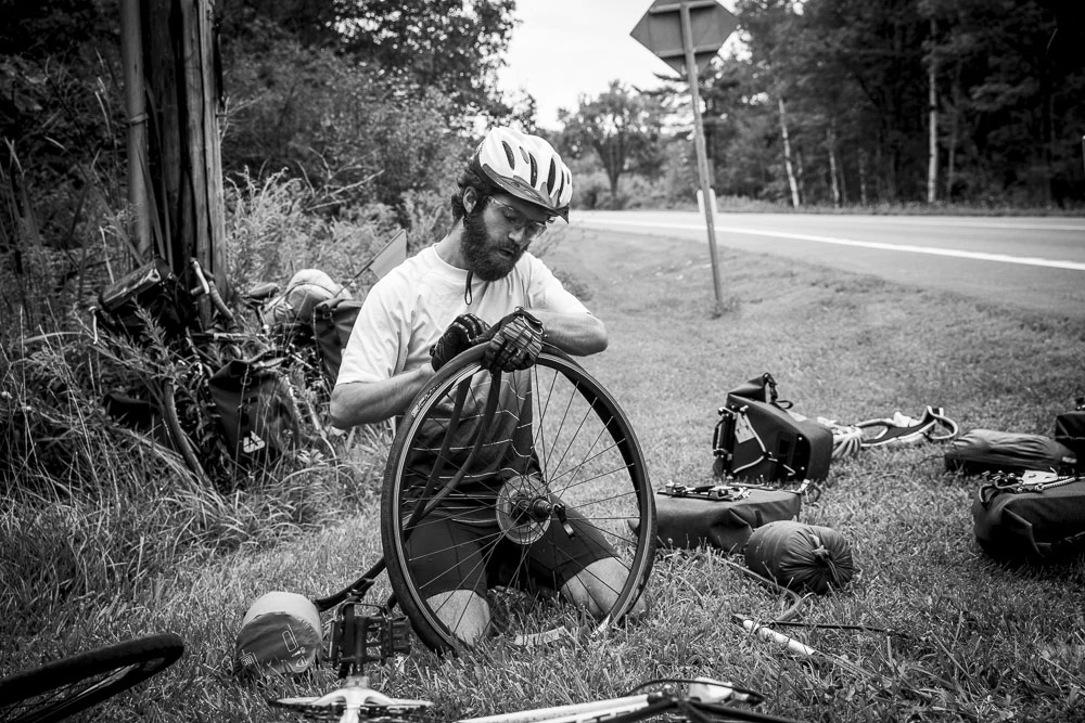 Mathieu qui répare une crevaison, la deuxième de la journée, sur le bon d’une route entre Malta et Stanford.